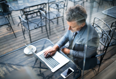 Mature businessman with laptop outside a cafe.